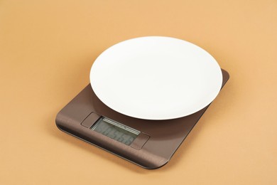 Photo of Electronic kitchen scale with empty plate on beige background, closeup