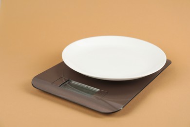 Photo of Electronic kitchen scale with empty plate on beige background, closeup