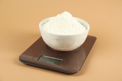 Photo of Electronic kitchen scale with bowl of flour on beige background, closeup