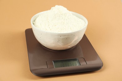 Photo of Electronic kitchen scale with bowl of flour on beige background, closeup