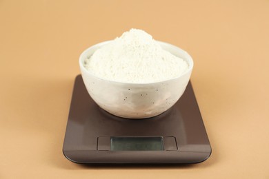 Photo of Electronic kitchen scale with bowl of flour on beige background, closeup