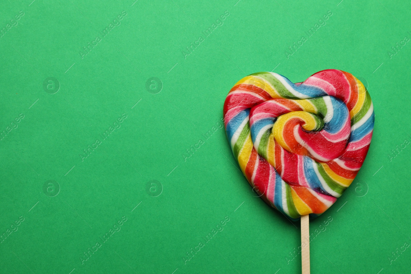 Photo of Tasty heart shaped lollipop on green background, top view. Space for text