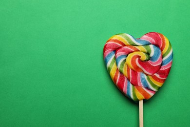 Tasty heart shaped lollipop on green background, top view. Space for text