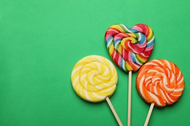 Photo of Tasty lollipops on green background, flat lay. Space for text