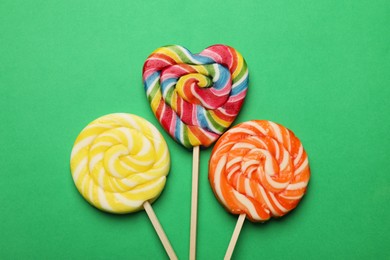 Tasty lollipops on green background, flat lay