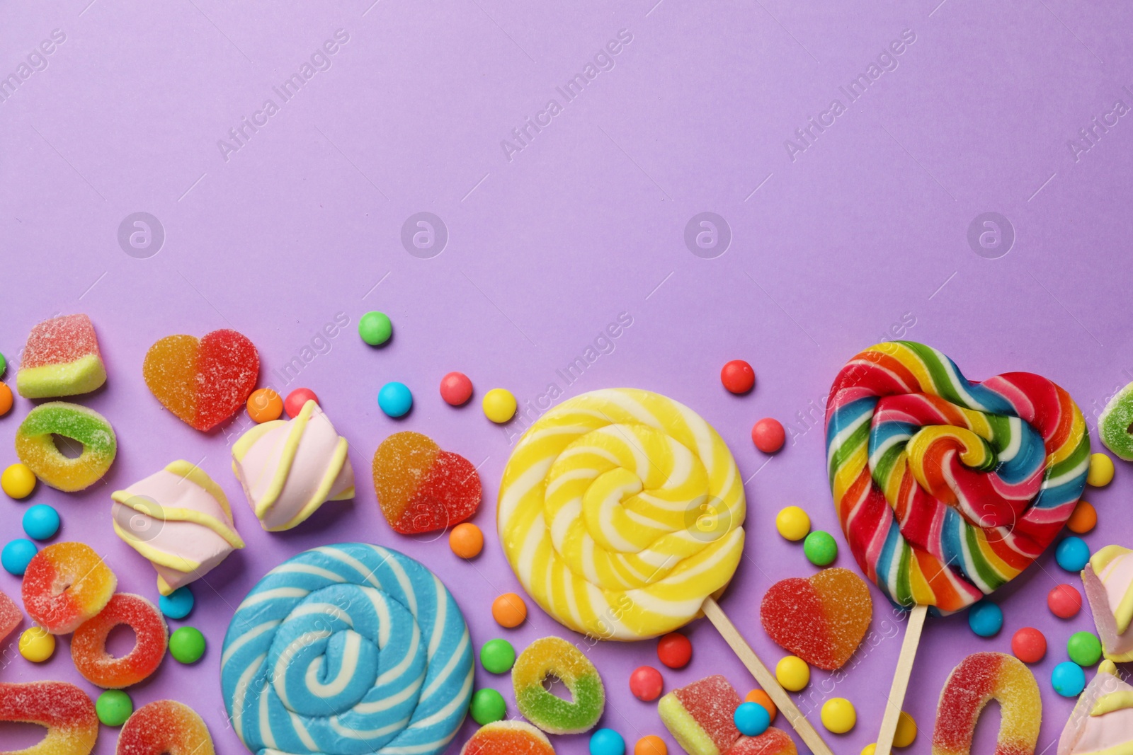 Photo of Many different tasty candies and marshmallows on violet background, flat lay. Space for text