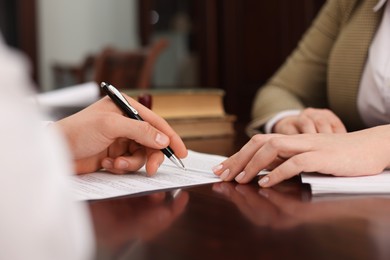 Photo of Notary and client signing document at table in office, closeup