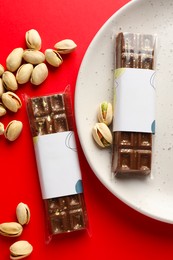 Photo of Delicious Dubai chocolate bars and pistachios on red background, flat lay