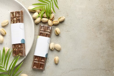 Photo of Delicious Dubai chocolate bars, pistachios and leaves on light background, flat lay. Space for text