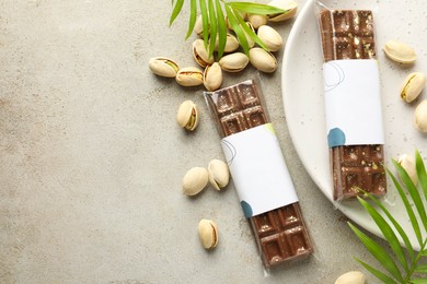 Photo of Delicious Dubai chocolate bars, pistachios and leaves on light background, flat lay. Space for text