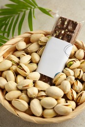 Photo of Delicious Dubai chocolate bar, pistachios and leaves on light background, closeup