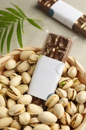 Photo of Delicious Dubai chocolate bars, pistachios and leaves on light background, closeup