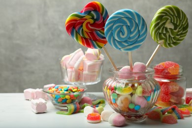 Different tasty candies on white table against grey background