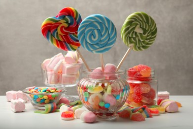 Photo of Different tasty candies on white table against grey background