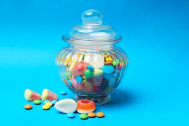 Different tasty candies in glass jar on light blue background, closeup