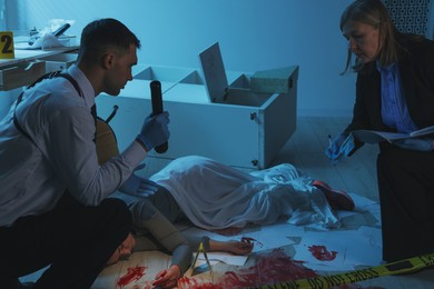 Photo of Forensic experts working at crime scene with dead woman's body indoors