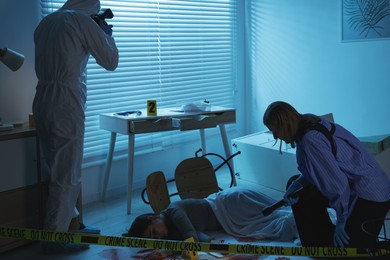 Forensic experts working at crime scene with dead woman's body indoors