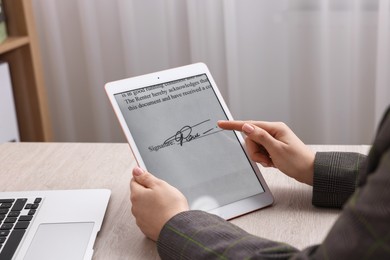 Photo of Electronic signature. Woman using tablet at wooden table indoors, closeup