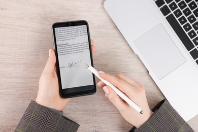 Electronic signature. Woman using stylus and smartphone at wooden table, top view