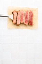 Photo of Delicious sliced beef tenderloin with different degrees of doneness on light tiled table, top view. Space for text