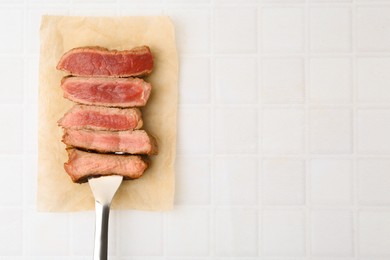 Photo of Delicious sliced beef tenderloin with different degrees of doneness on light tiled table, top view. Space for text