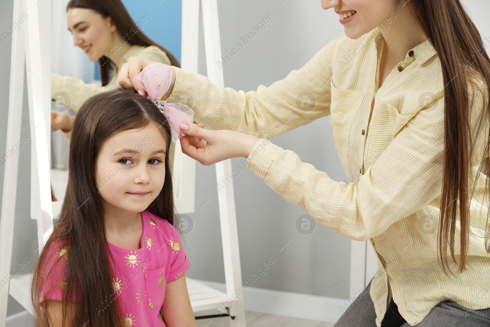 Photo of Mom putting cute accessories onto her daughter's hair at home, closeup