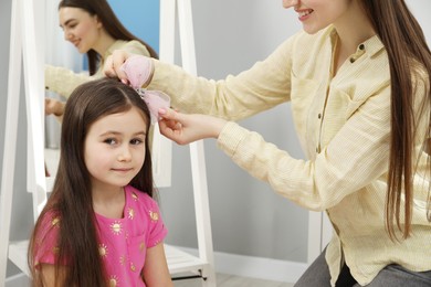 Mom putting cute accessories onto her daughter's hair at home, closeup