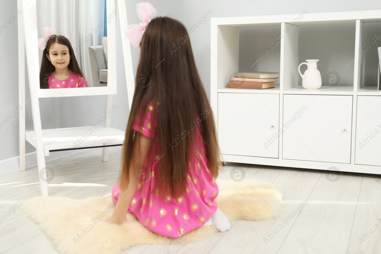 Photo of Little girl wearing beautiful hair clip near mirror at home