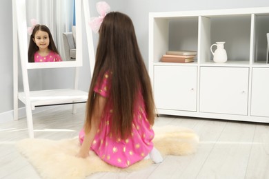 Little girl wearing beautiful hair clip near mirror at home