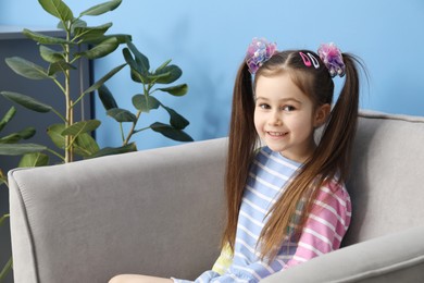 Photo of Happy little girl wearing beautiful hair accessories in armchair at home