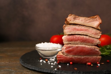 Photo of Delicious sliced beef tenderloin with different degrees of doneness and spices on table against brown background, closeup. Space for text