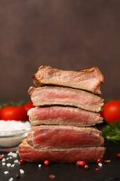 Photo of Delicious sliced beef tenderloin with different degrees of doneness and spices on table against brown background, closeup