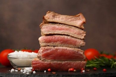 Photo of Delicious sliced beef tenderloin with different degrees of doneness and spices on table against brown background, closeup