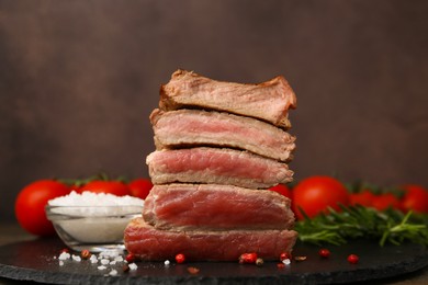 Photo of Delicious sliced beef tenderloin with different degrees of doneness and spices on table against brown background