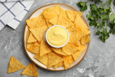Photo of Tasty cheese dipping sauce in bowl, nacho chips and parsley on grey table, flat lay