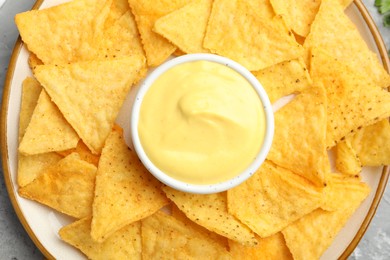 Photo of Tasty cheese dipping sauce in bowl and nacho chips on table, top view
