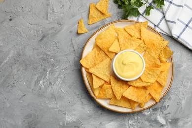 Photo of Tasty cheese dipping sauce in bowl, nacho chips and parsley on grey table, flat lay. Space for text