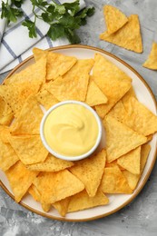 Photo of Tasty cheese dipping sauce in bowl, nacho chips and parsley on grey table, flat lay