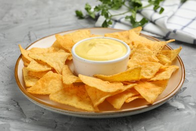 Photo of Tasty cheese dipping sauce in bowl, nacho chips and parsley on grey table, closeup