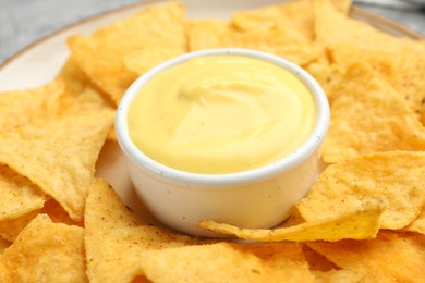 Photo of Tasty cheese dipping sauce in bowl and nacho chips on table, closeup