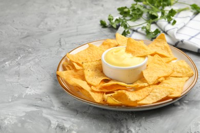 Photo of Tasty cheese dipping sauce in bowl, nacho chips and parsley on grey table, closeup. Space for text