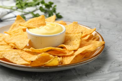 Photo of Tasty cheese dipping sauce in bowl, nacho chips and parsley on grey table, closeup