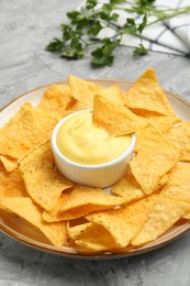 Photo of Tasty cheese dipping sauce in bowl, nacho chips and parsley on grey table, closeup