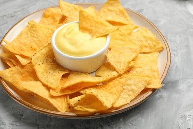 Photo of Tasty cheese dipping sauce in bowl and nacho chips on grey table, closeup