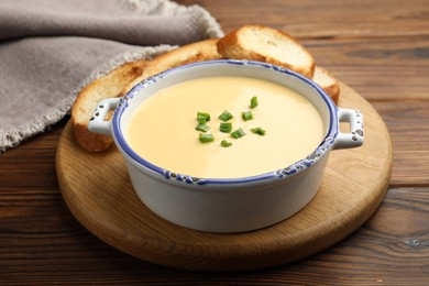 Photo of Tasty cheese dipping sauce in bowl and croutons on wooden table, closeup