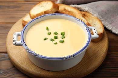 Photo of Tasty cheese dipping sauce in bowl and croutons on wooden table, closeup