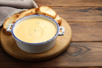 Photo of Tasty cheese dipping sauce in bowl and croutons on wooden table, closeup. Space for text