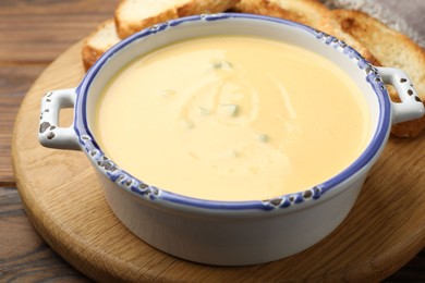 Photo of Tasty cheese dipping sauce in bowl and croutons on wooden table, closeup