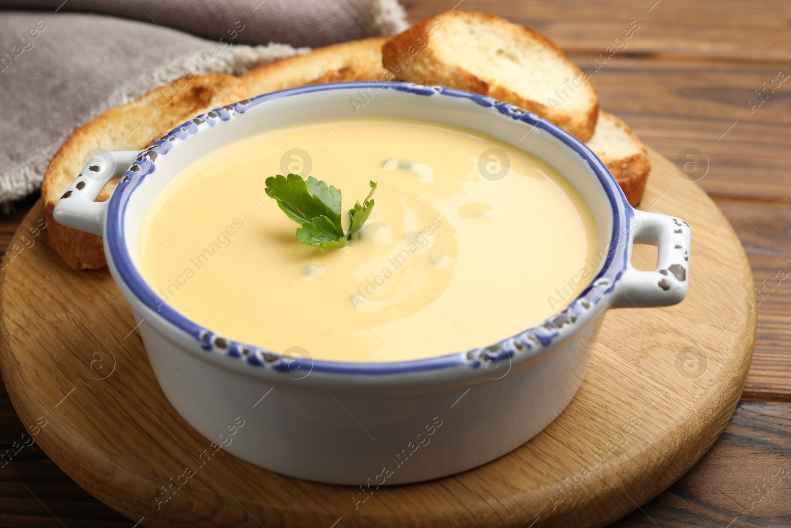 Photo of Tasty cheese dipping sauce in bowl and croutons on wooden table, closeup