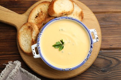 Photo of Tasty cheese dipping sauce in bowl and croutons on wooden table, top view